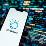 Hand holding a mobile phone with the IBM Watson logo on display on a background of program codes.
