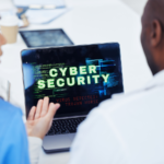 Two IT professionals discussing infront of a laptop with cybersecurity alert warning on display.