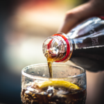 A bottle of Coca Cola being poured on a glass.