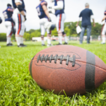 Close up of a football on a field with players on the background.