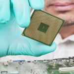 A person holding an processor chip atop a circuit board.