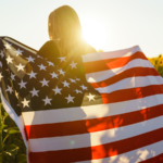 Girl with the US flag on a field of sunflowers.