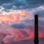Industrial chimney stack silhouette against a cloudy sky background.