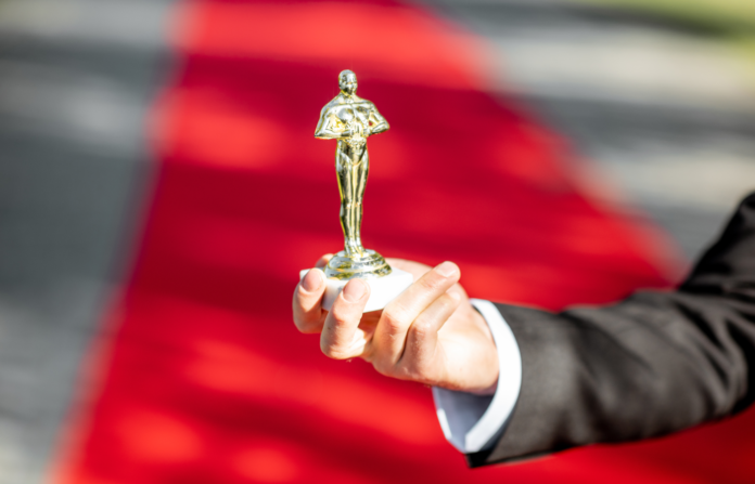 Person holding an award statue on a red carpet walk background.