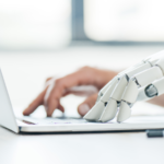 A human hand and a robotic hand operating a laptop.
