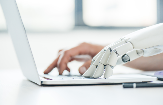 A human hand and a robotic hand operating a laptop.