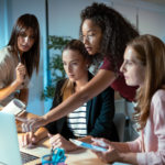 Four businesswomen talking and reviewing the latest work done on the computer in a joint workspace.