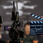 Back view of a cameraman and a hand holding a board clapper.