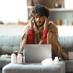 Sick man covered in blanket and sitting on a couch at home.