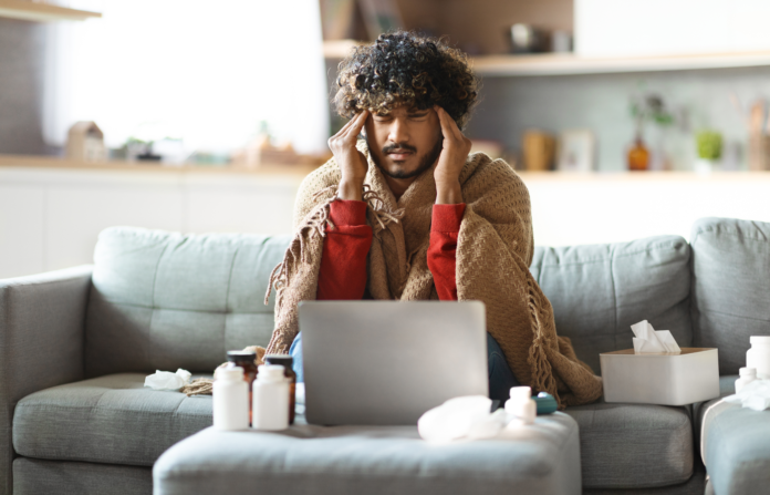 Sick man covered in blanket and sitting on a couch at home.