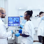 African assitant discussing wtih scientist about virus experiment in chemistry laboratory.