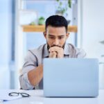 Stock image of a worker who appears to be stressed looking at his laptop.