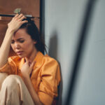 Unhappy young lady sitting on the floor at home.