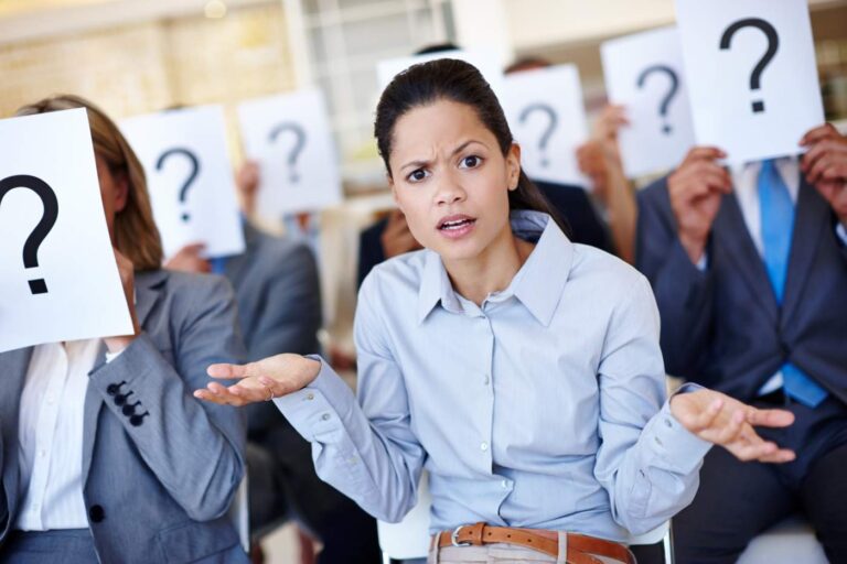 Shot of a group of businesspeople holding up signs with question marks on them during a work presentation while their colleague looks confused.