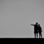 Black and white photo of silhuettes, one pointing in a direction.
