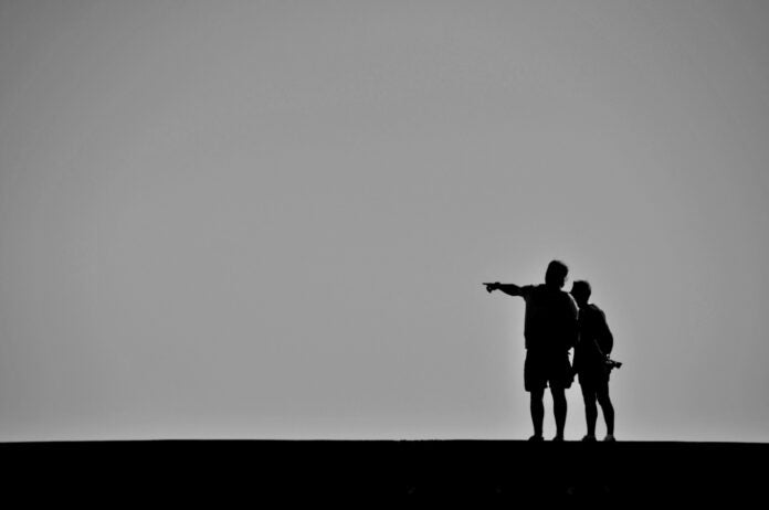 Black and white photo of silhuettes, one pointing in a direction.