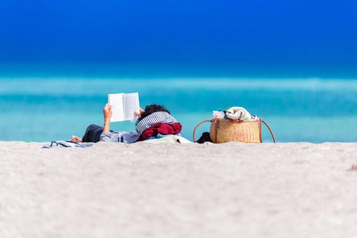 A person lying on shore reading a book.