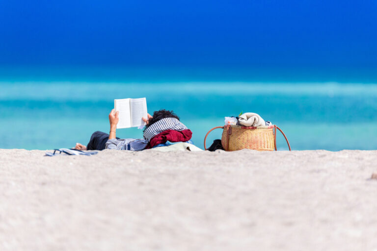 A person lying on shore reading a book.