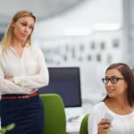 Stock photo of two workers in an office with one person appearing to look at the other with judgment.