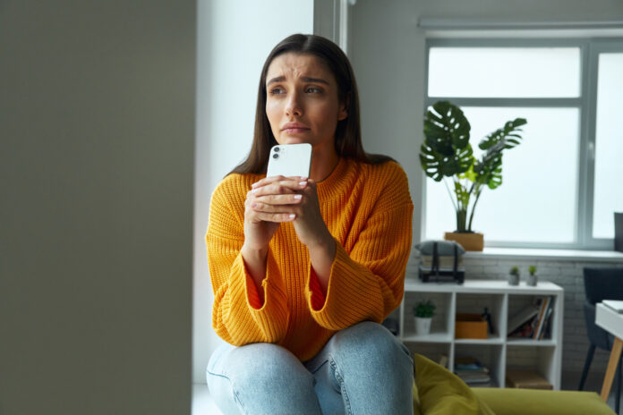 A woman looks far as she holds her smartphone.