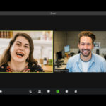 Man in blue dress shirt smiling beside woman in black and red floral dress while in Zoom meeting.