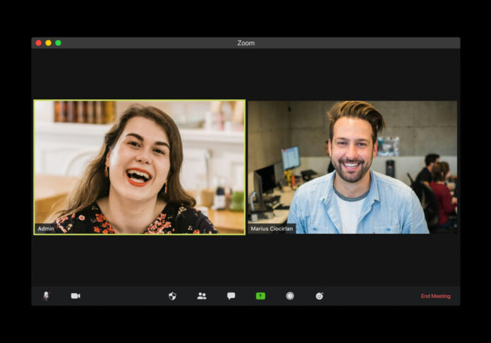 Man in blue dress shirt smiling beside woman in black and red floral dress while in Zoom meeting.