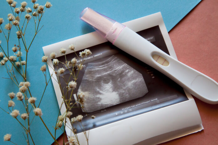 Ultrasound scan of an unborn baby of fifth week with a pregnancy test on the blue-pink background.